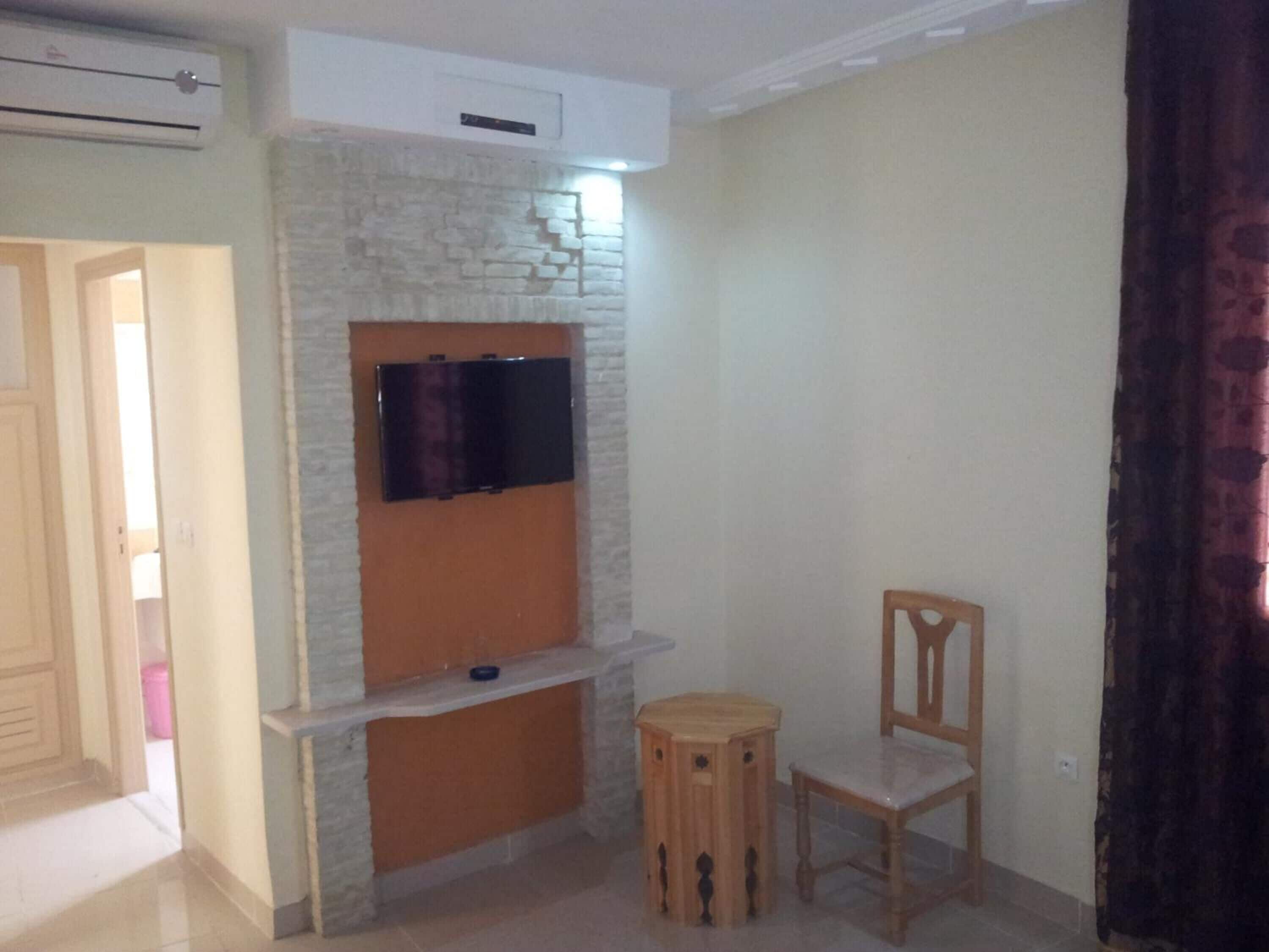 Quarto com parede de pedra, televisão de tela plana montada, cadeira de madeira e mesa redonda pequena.