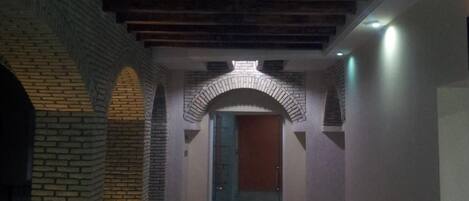 Un pasillo con arcos de ladrillo, techo de madera y una puerta al final.