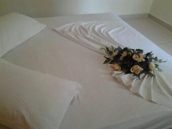 Una cama bien hecha con sábanas blancas y un arreglo floral sobre ella.