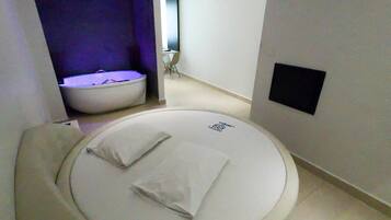 Quarto de hotel moderno com uma cama redonda, um espaço de estar pequeno e um design minimalista.