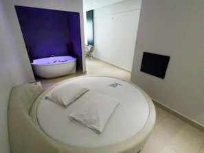 Una habitación de hotel moderna con una cama redonda, una pequeña zona de estar y un diseño minimalista.
