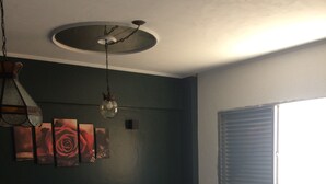 Een kamer met een rond bed, een eettafel, een plafondventilator en een raam met jaloezieën.