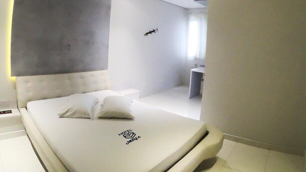 Een moderne slaapkamer met een gebogen plafond, een bed met een logo, een klein nachtkastje en een nachtkastje.