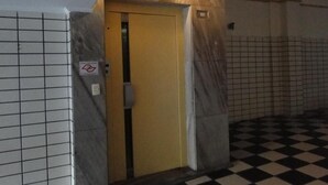 Een hotelkamer met een zwart-wit geruite vloer, een gele deur en een bordje met een rookverbod.