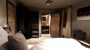 Un dormitorio con cama, armario, espejo y una mesita.