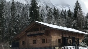 Una cabaña de madera con balcón, rodeada de árboles nevados y montañas.