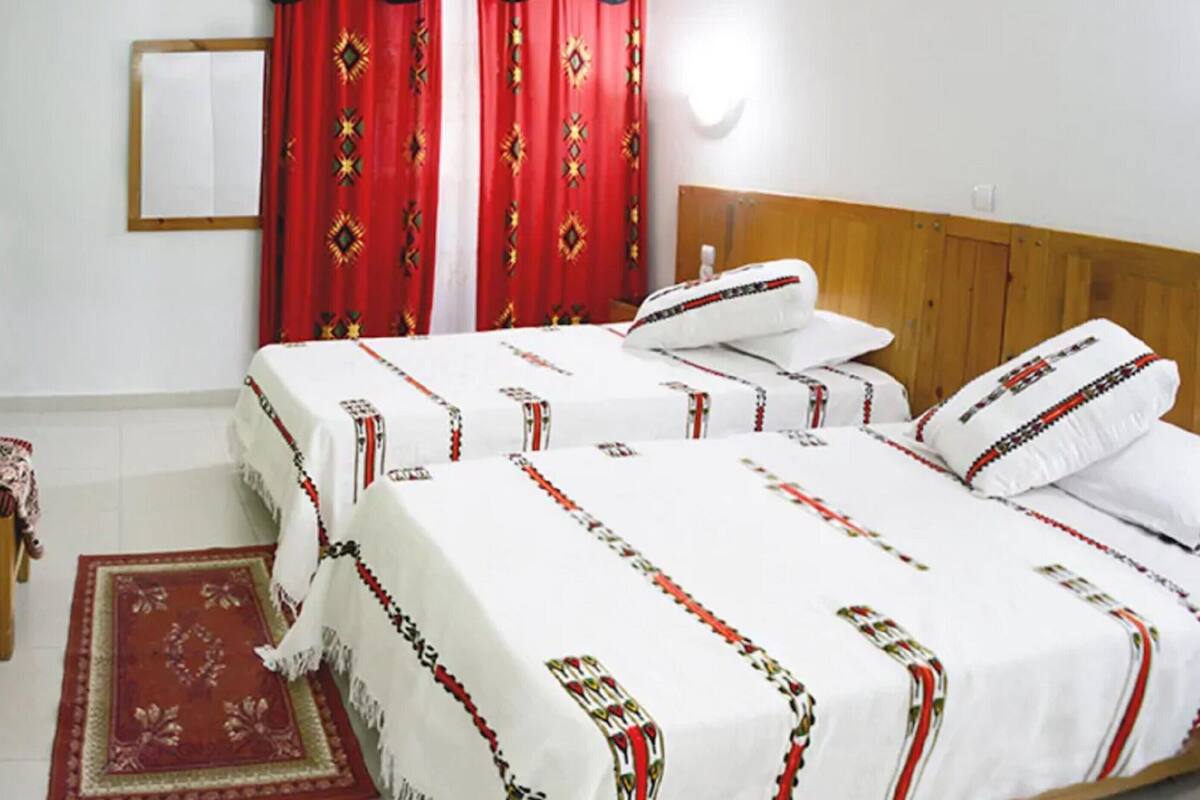 Uma cama de casal com colcha branca e cortinas vermelhas.