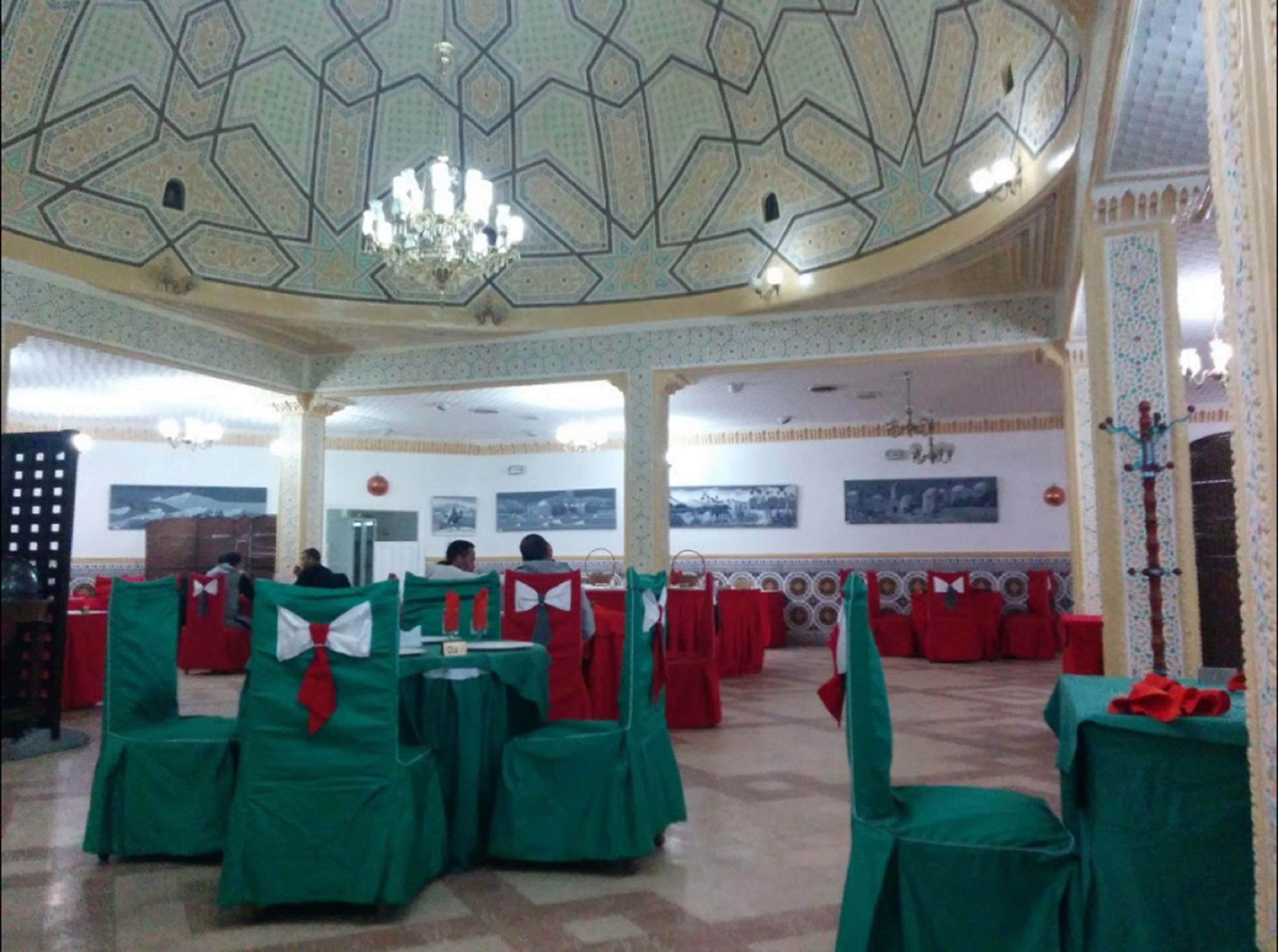 Une salle avec des tables recouvertes de nappes vertes et rouges, un plafond orné de motifs et des tableaux accrochés aux murs.