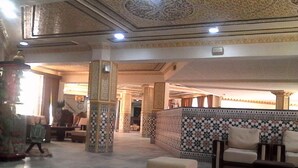 Un vestíbulo espacioso con columnas ornamentales, un diseño de pared llamativo y un área de descanso con otomanas.