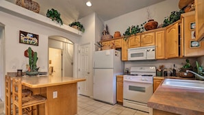 A kitchen with wooden cabinets, a white refrigerator, a microwave, and a stove. There are plants on the shelves and a wicker basket on the counter.