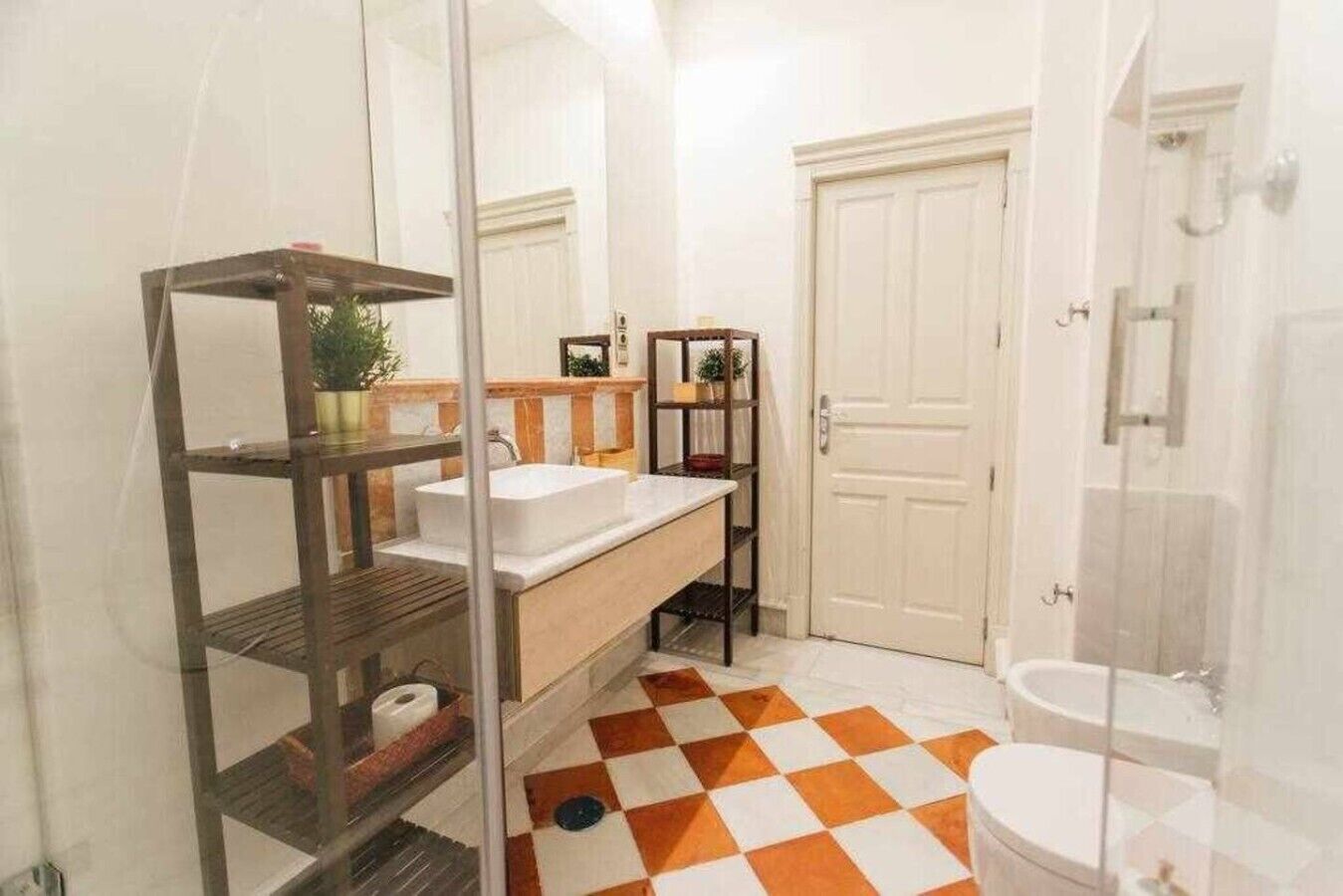 A bathroom with a checkered floor, a white sink, a glass shower enclosure, and a white door.