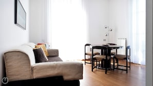 Un saló modern amb un sofà, una taula de dinar amb caires i una làmpada de peu.