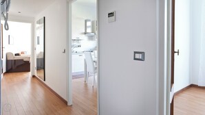 Un interior modern amb un terra de fusta, una cuina amb armaris blancs i una zona de menjador amb una cadira blanca.