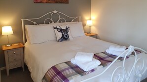 A neatly made bed with a plaid blanket and two towels, a white headboard, bedside lamps, a nightstand with drawers, and a painting above the bed. - Beautiful views, walking distance to town (Pitlochry)