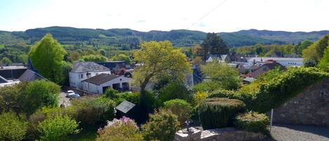 A residential area with houses, a stone wall, and a view of green hills in the background.