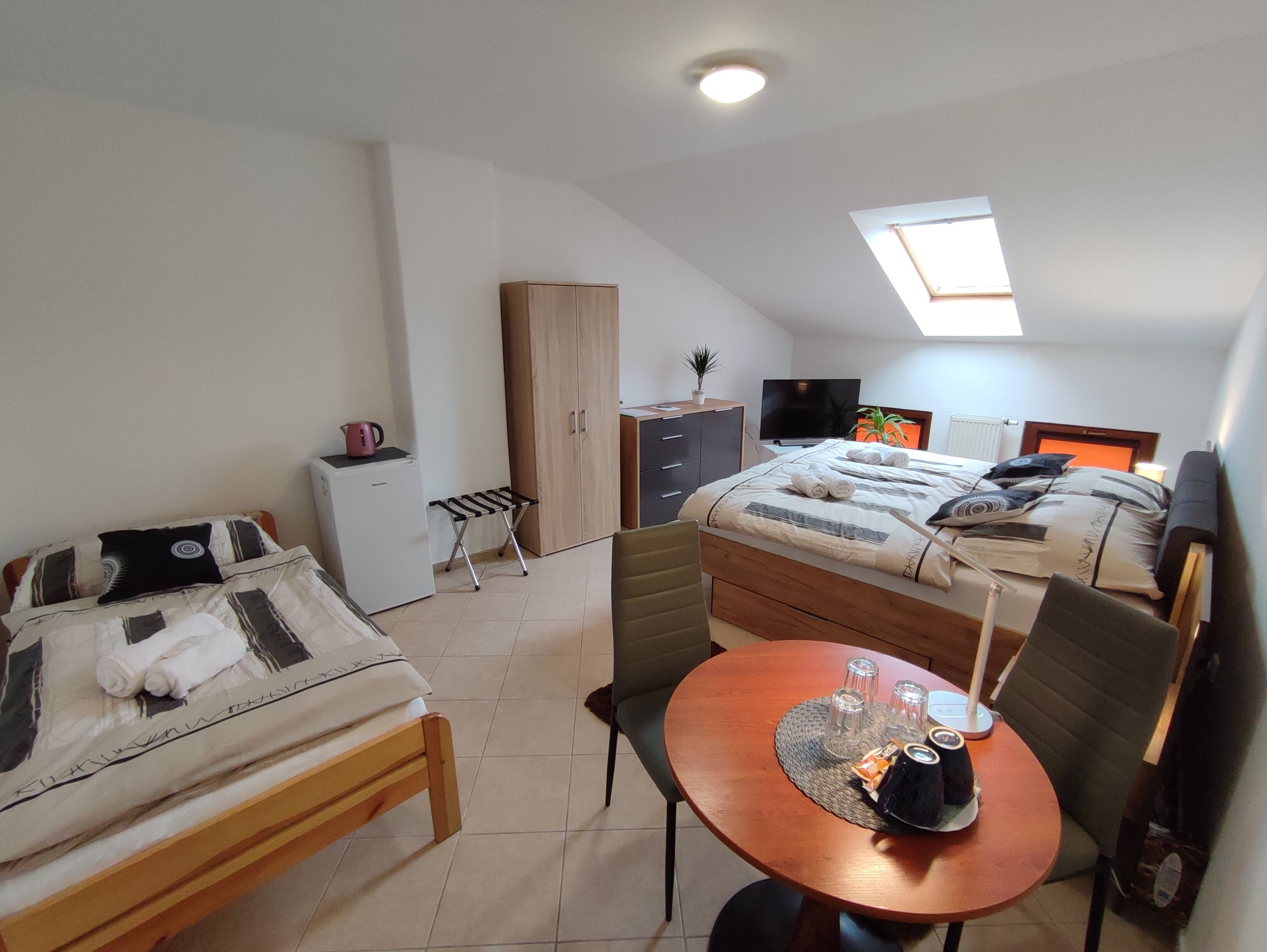 A compact bedroom with a bed, a small desk, a chair, a wardrobe, a television, and a skylight.