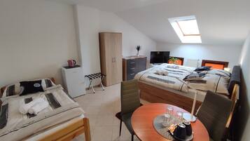 A compact bedroom with a bed, a small desk, a chair, a wardrobe, a television, and a skylight.