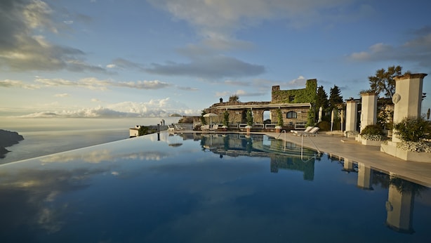 An infinity pool with a clear view of the ocean and a historic building in the background. - Villa Margherita (Ravello)
