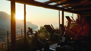 A gym with stationary bikes and a view of a valley at sunset. - Villa Margherita (Ravello)
