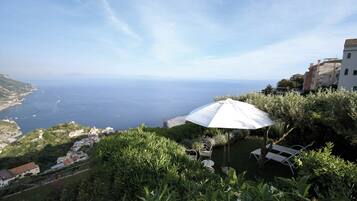 Vista sulla costa con un ombrellone bianco, vegetazione e edifici sullo sfondo.