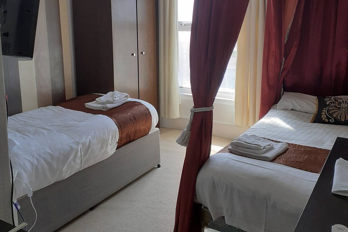 A hotel room with two beds, a wardrobe, a TV, and a window with curtains.