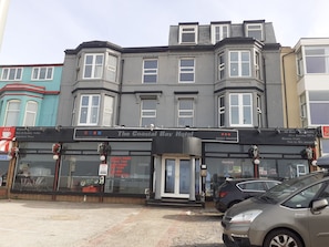 The Coastal Bay Hotel with a black facade, multiple windows, and a signboard advertising services like a beauty salon and rooms for two to six people.