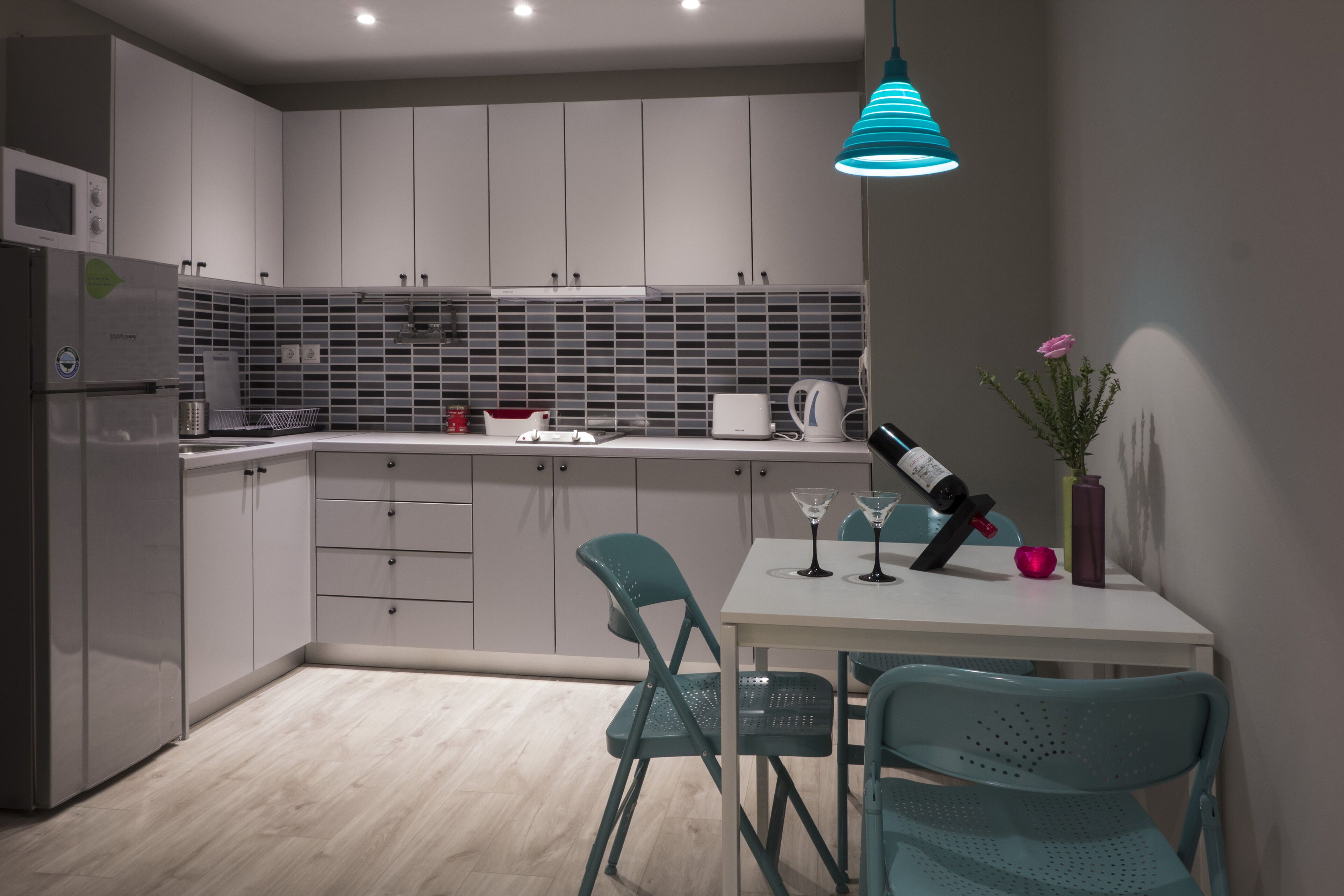 A modern kitchen with grey cabinets, a white countertop, and teal chairs.