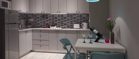 A modern kitchen with grey cabinets, a white countertop, and teal chairs.