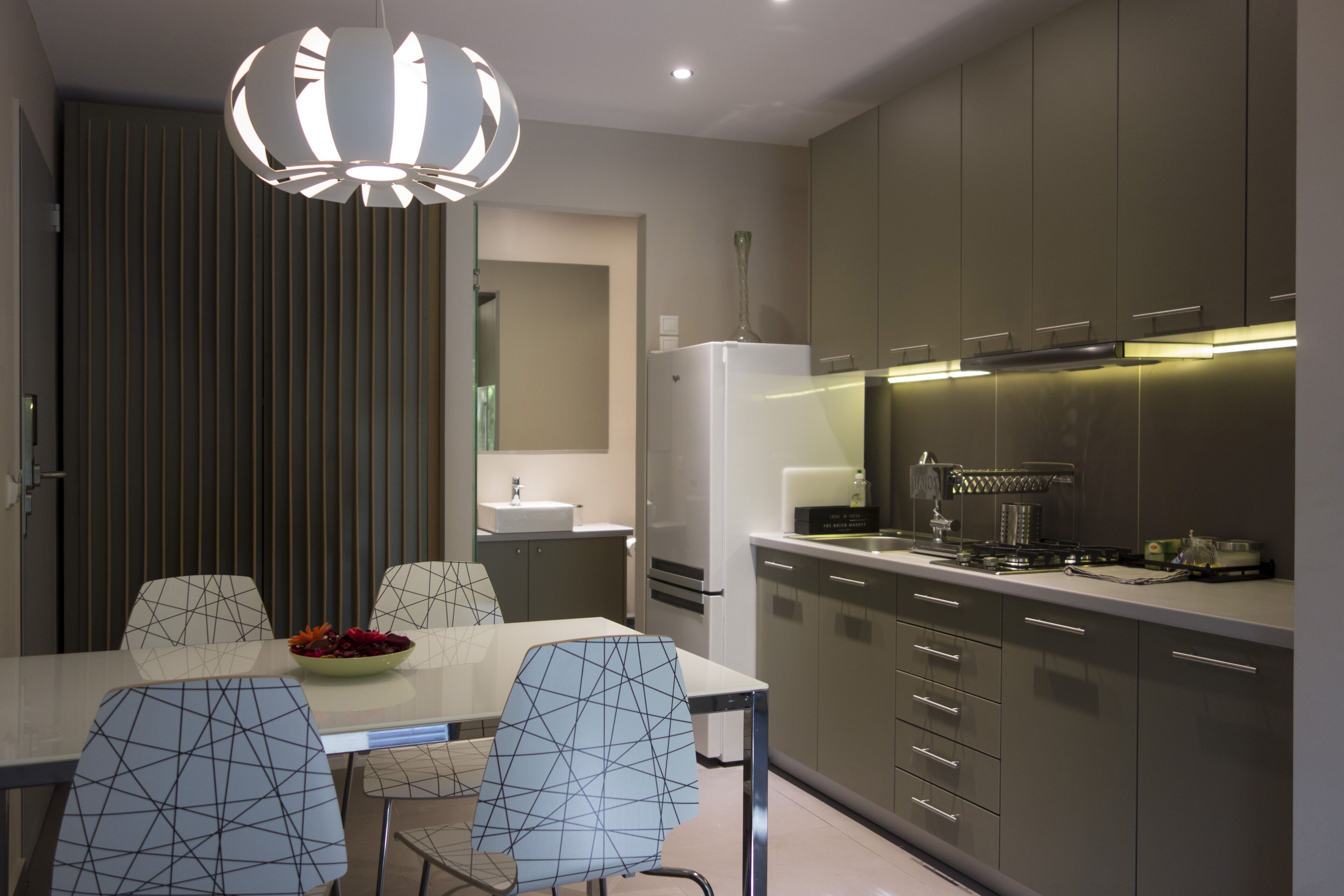 A modern kitchen with a dining area, featuring a large island, contemporary chairs, and a stylish pendant light.
