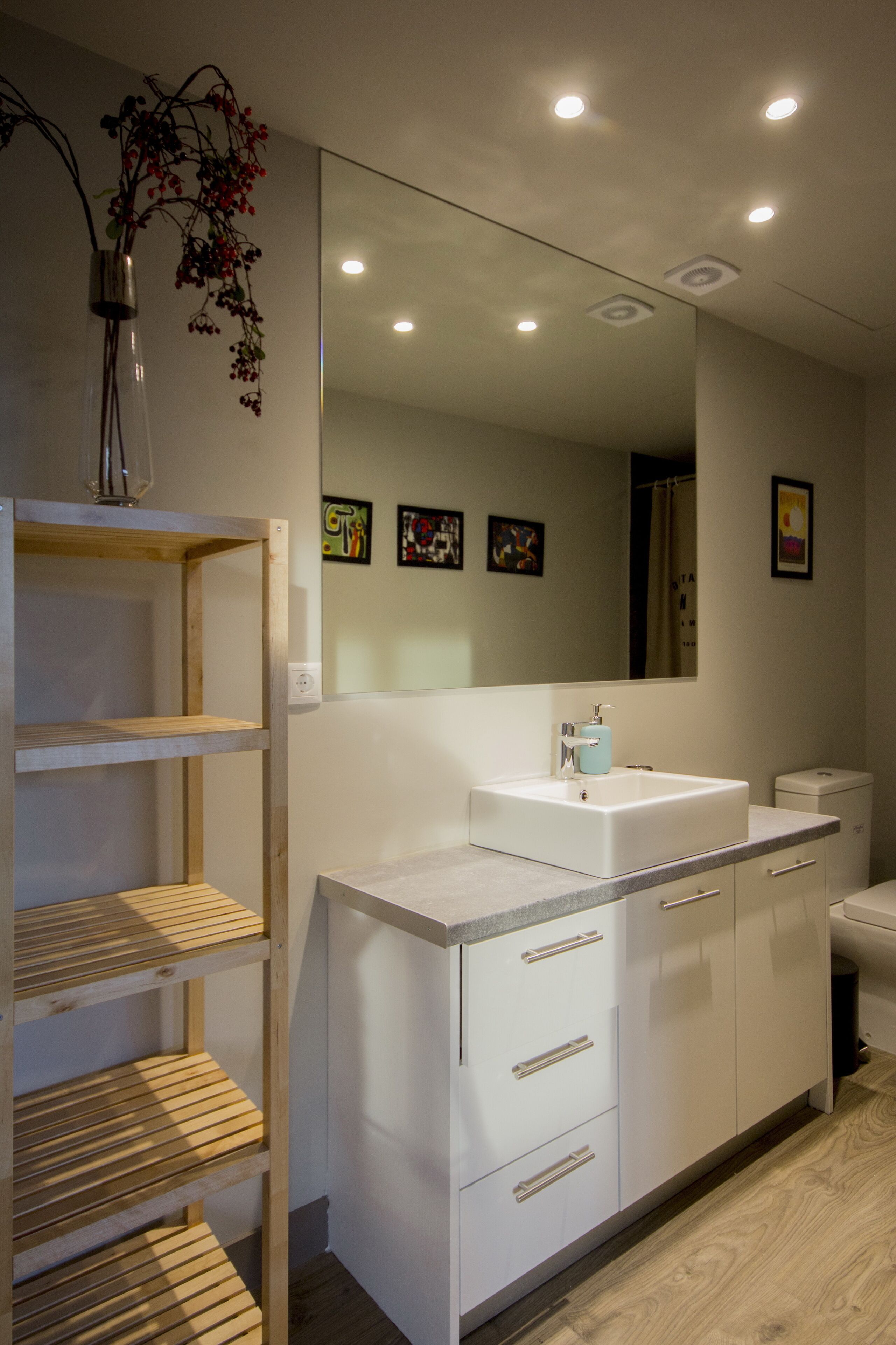 A modern bathroom with a white sink, mirror, and wooden shelving unit.