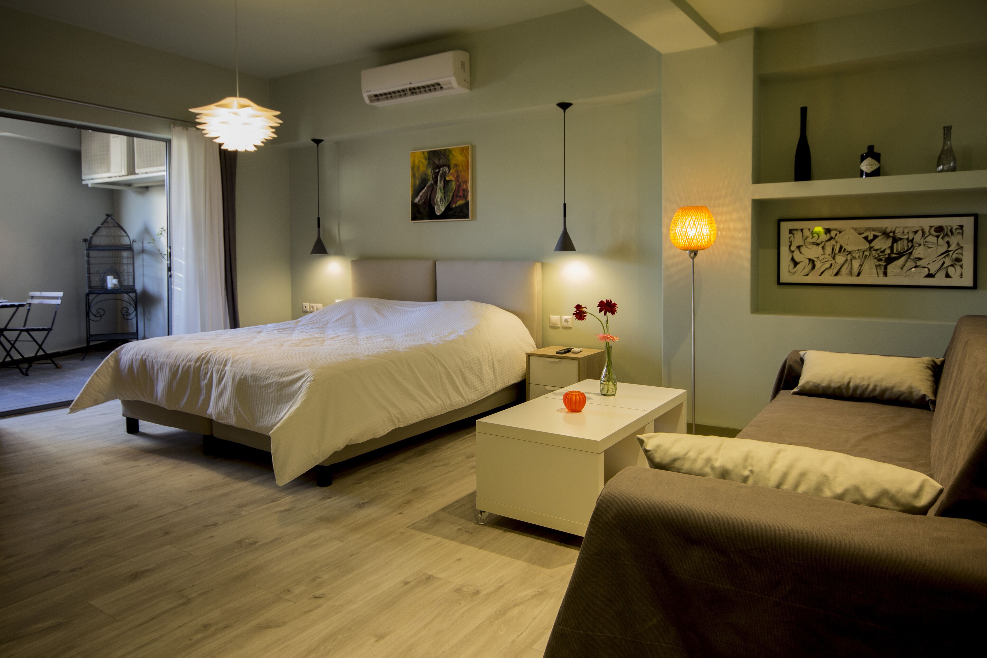 A modern hotel room with a bed, a sofa, a bedside table, and a lamp.