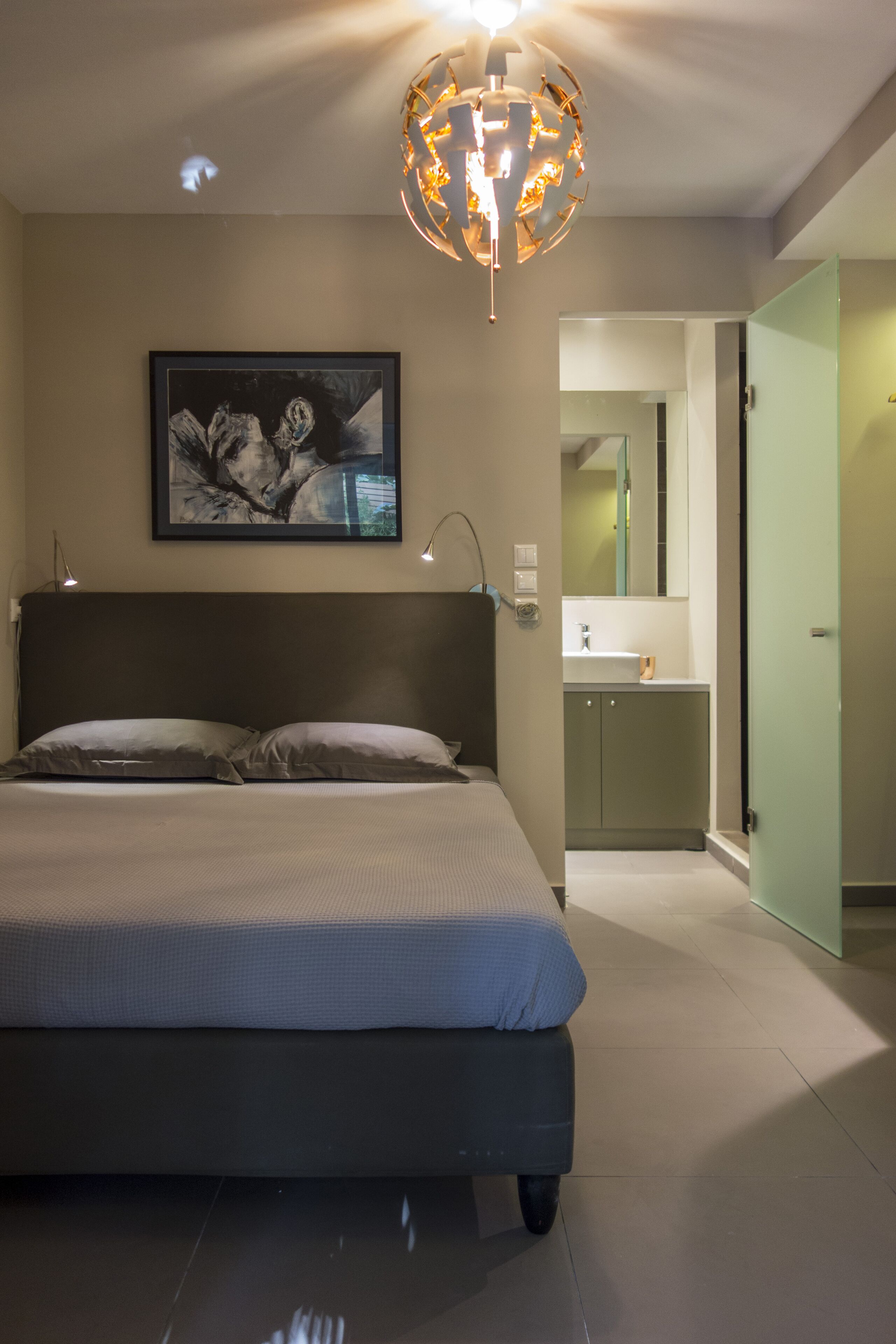 A modern bedroom with a large bed, a ceiling light fixture, and a framed artwork on the wall.