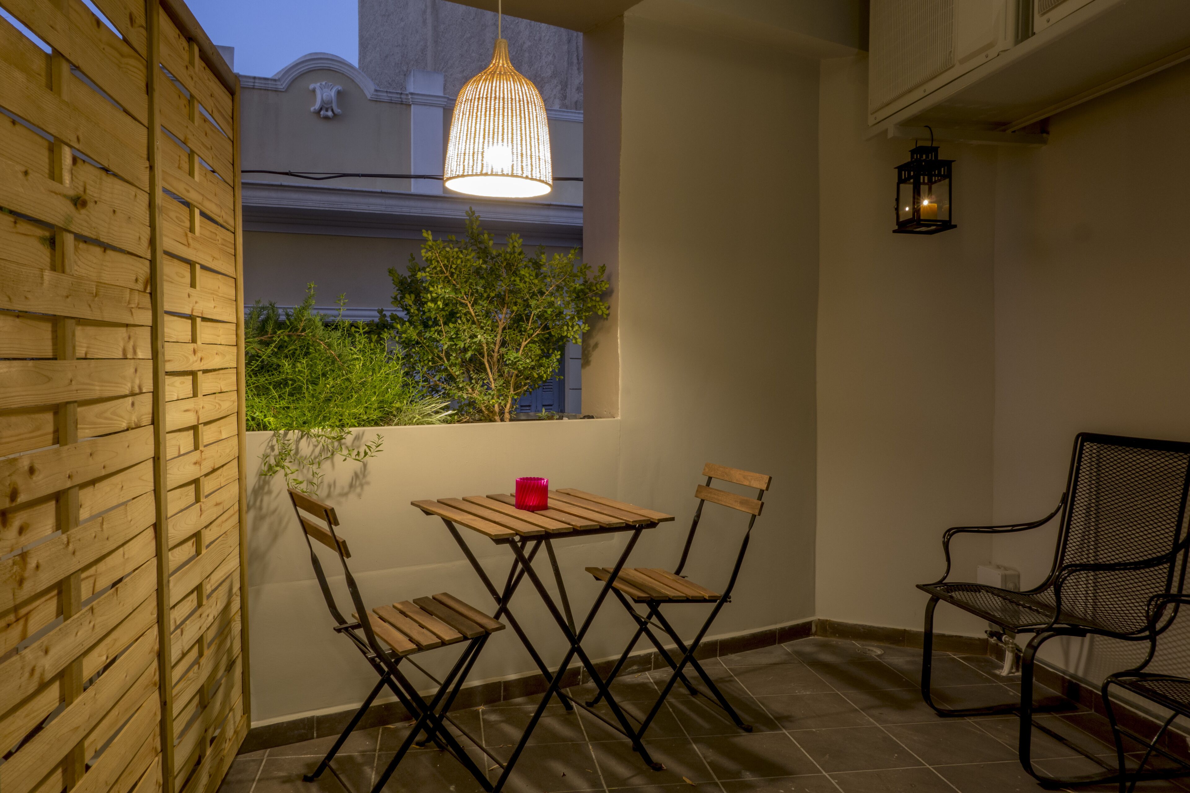 A small patio with a wooden table and chairs, a hanging light fixture, and a wall-mounted lantern.