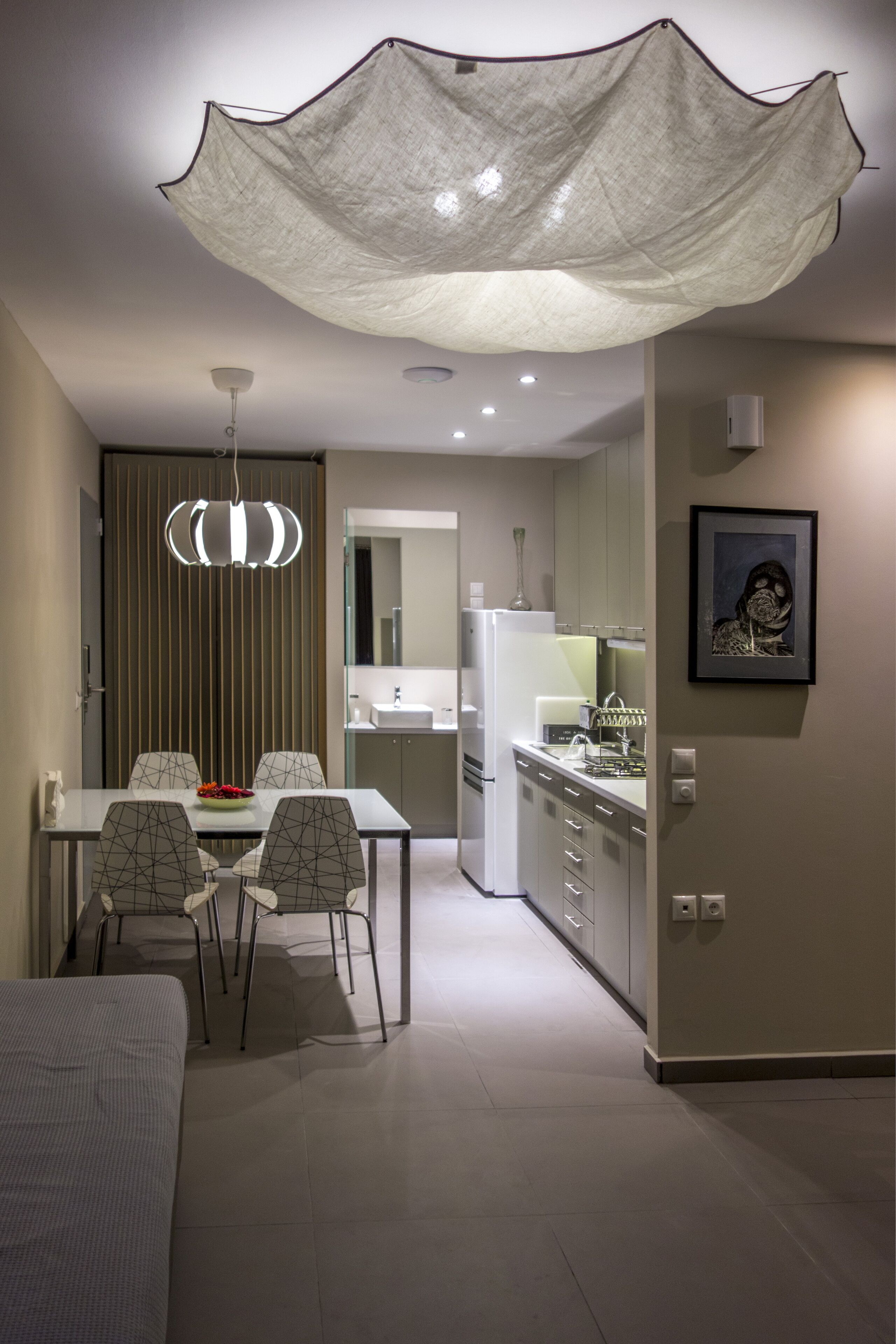 A modern kitchen with a dining area, featuring a large chandelier, a refrigerator, and a framed artwork on the wall.