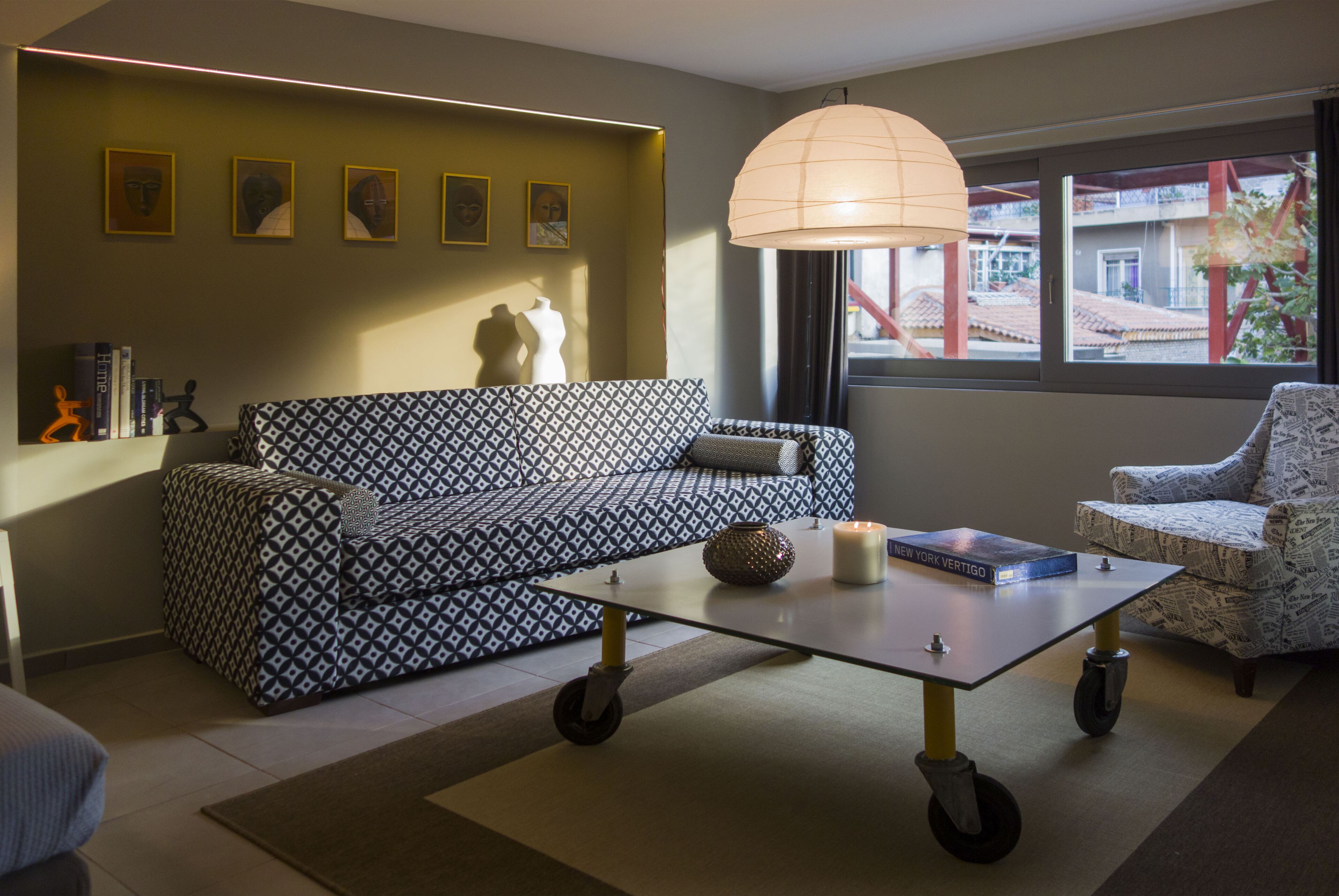 A modern living room with a patterned sofa, a coffee table, and a large window with a view of buildings.