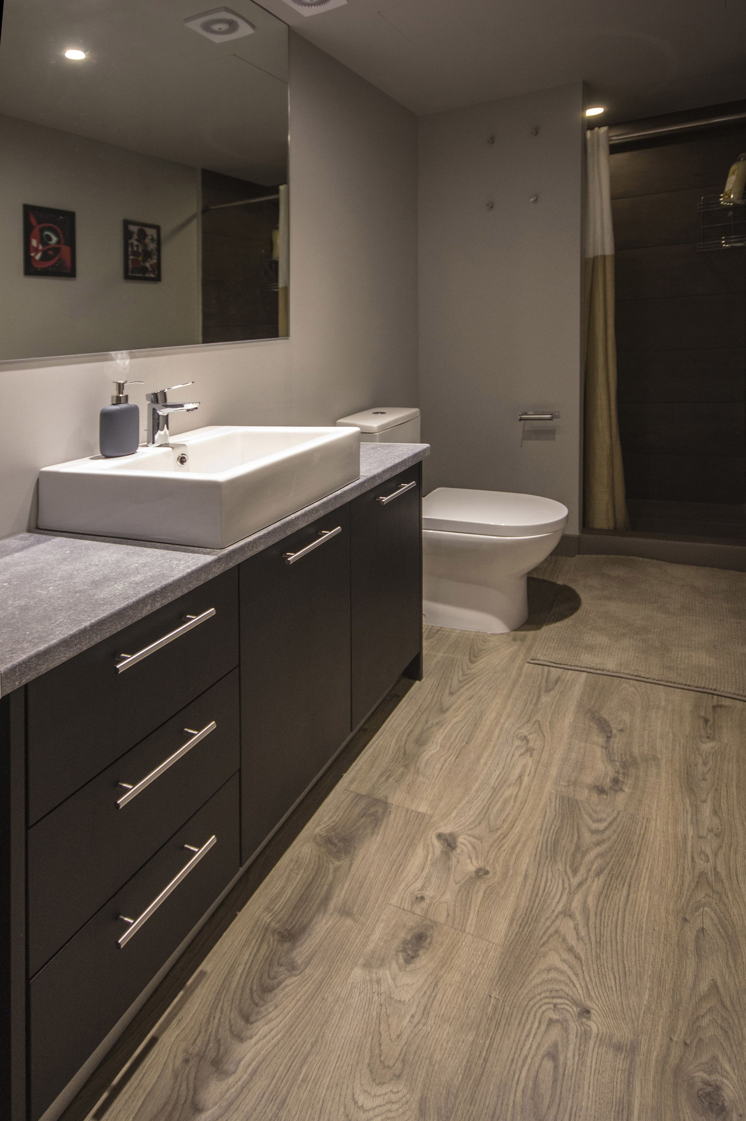 Un baño moderno con un espejo grande, muebles oscuros, un lavamanos blanco y un inodoro.