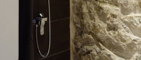 A shower with a handheld showerhead and a wall-mounted faucet.