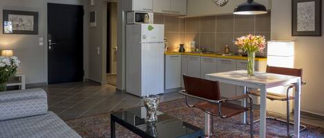A modern kitchen with a refrigerator, microwave, and a clock on the wall. There is a dining table with chairs and a vase with flowers.