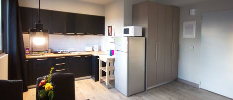 A modern kitchen with dark cabinets, a microwave, a refrigerator, and a dining area with a table and chairs.