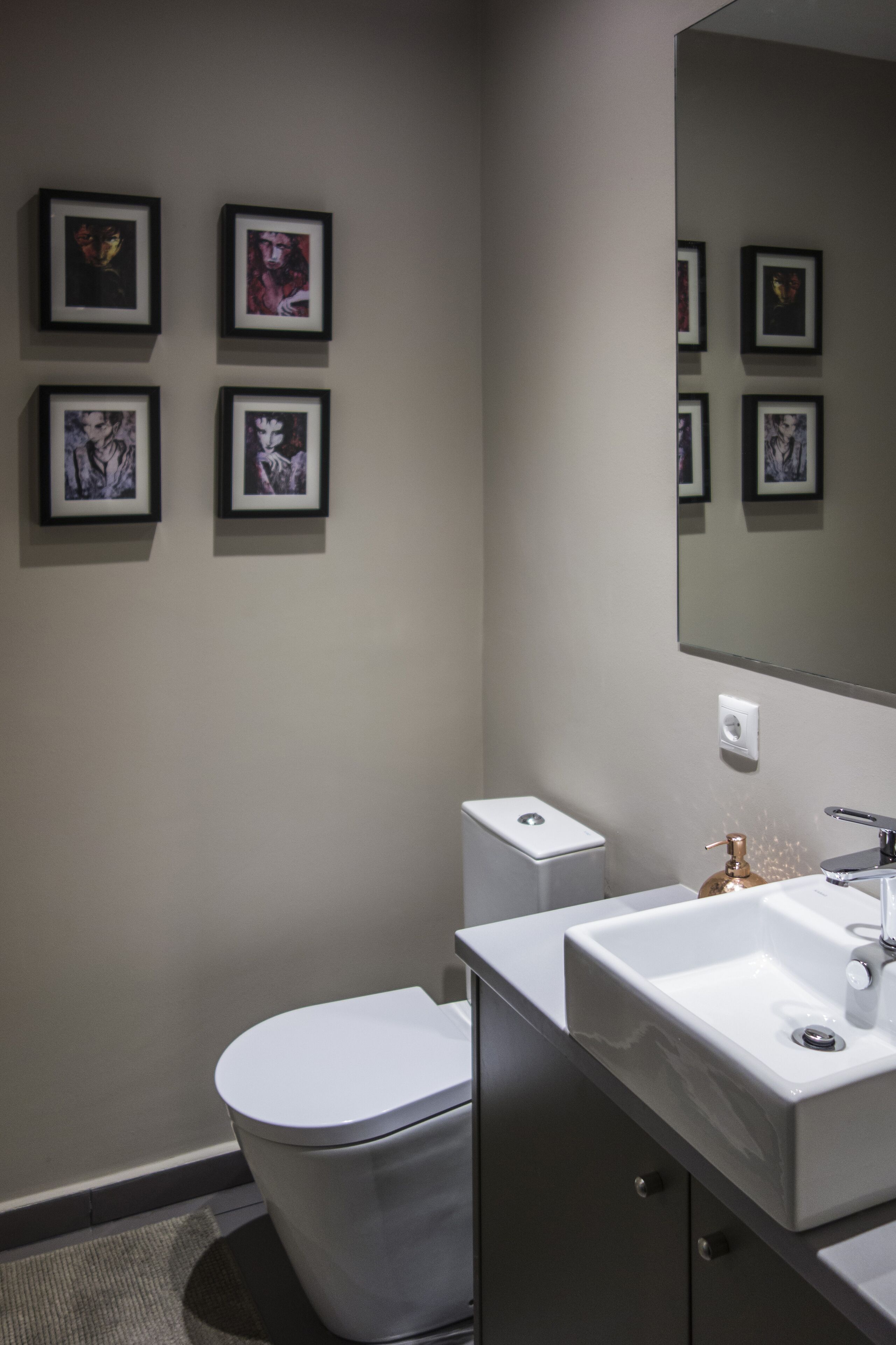 A modern bathroom with a toilet, sink, and framed artwork on the wall.