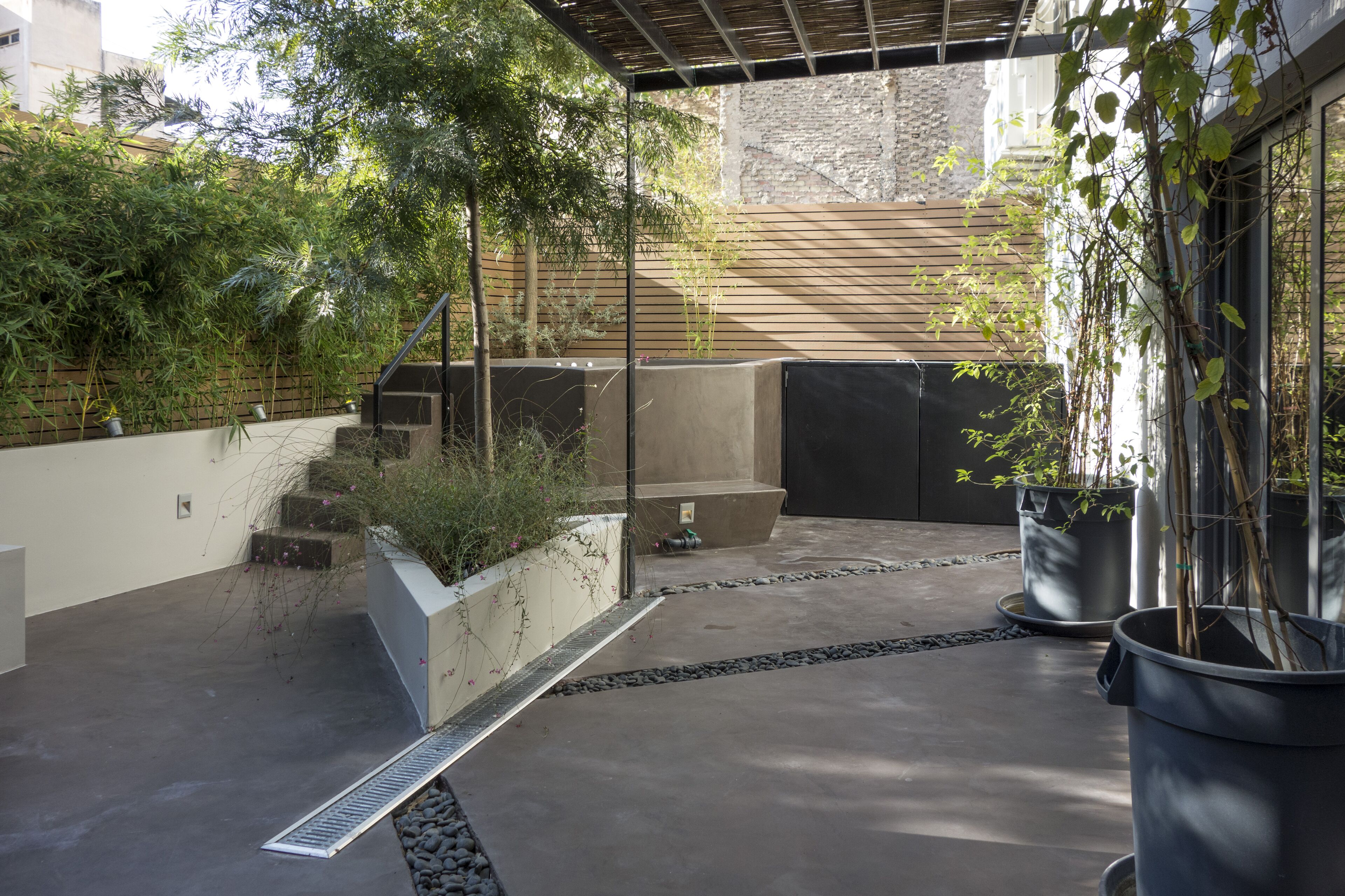 Un espace patio extérieur moderne, doté d’un sol en béton, de plantes en pot et d’une pergola en bois.