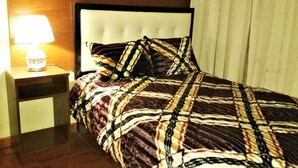 Ein Hotelzimmer mit Bett, Nachttisch, Lampe und einem Fenster mit Vorhängen.