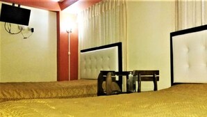 Ein Hotelzimmer mit einem großen Bett, einem kleinen Tisch, einem Sessel sowie einem an der Wand befestigten Fernseher und einem Vorhang.