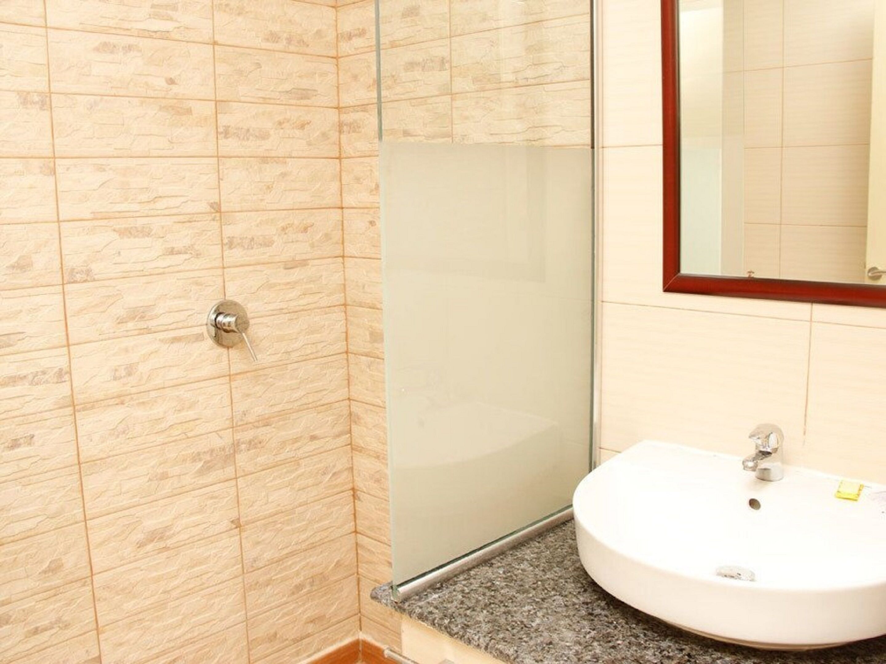 A bathroom with a glass shower enclosure, a sink with a mirror, and tiled walls.