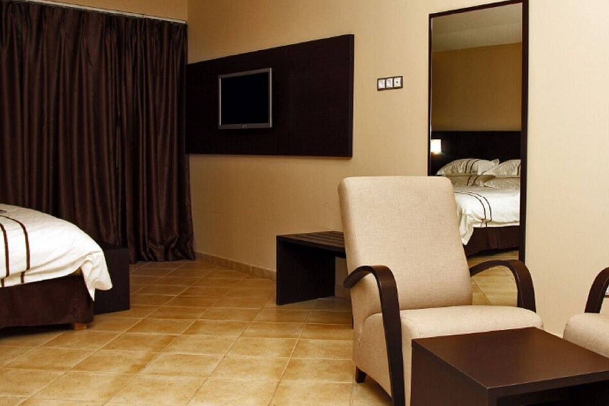 A hotel room with two beds, a TV mounted on the wall, a chair, a small table, and a mirror.