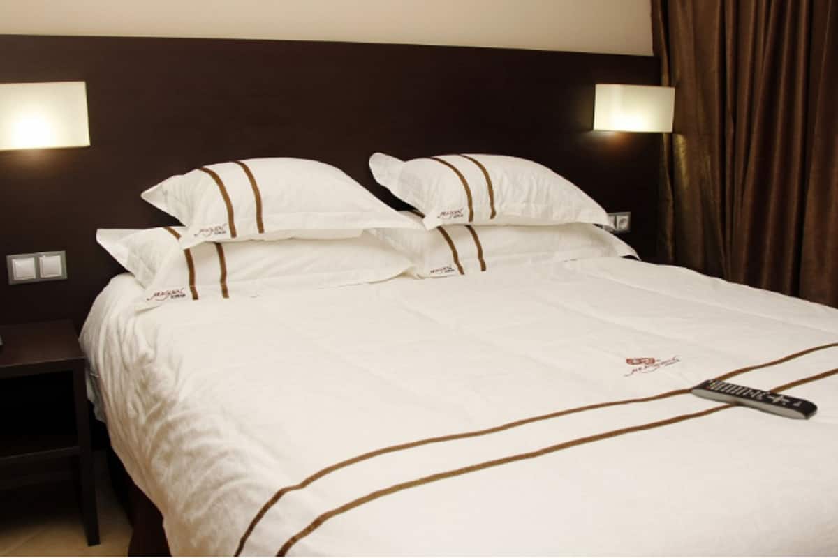 A hotel room with a large bed, two bedside lamps, a telephone, and a remote control on the bed.