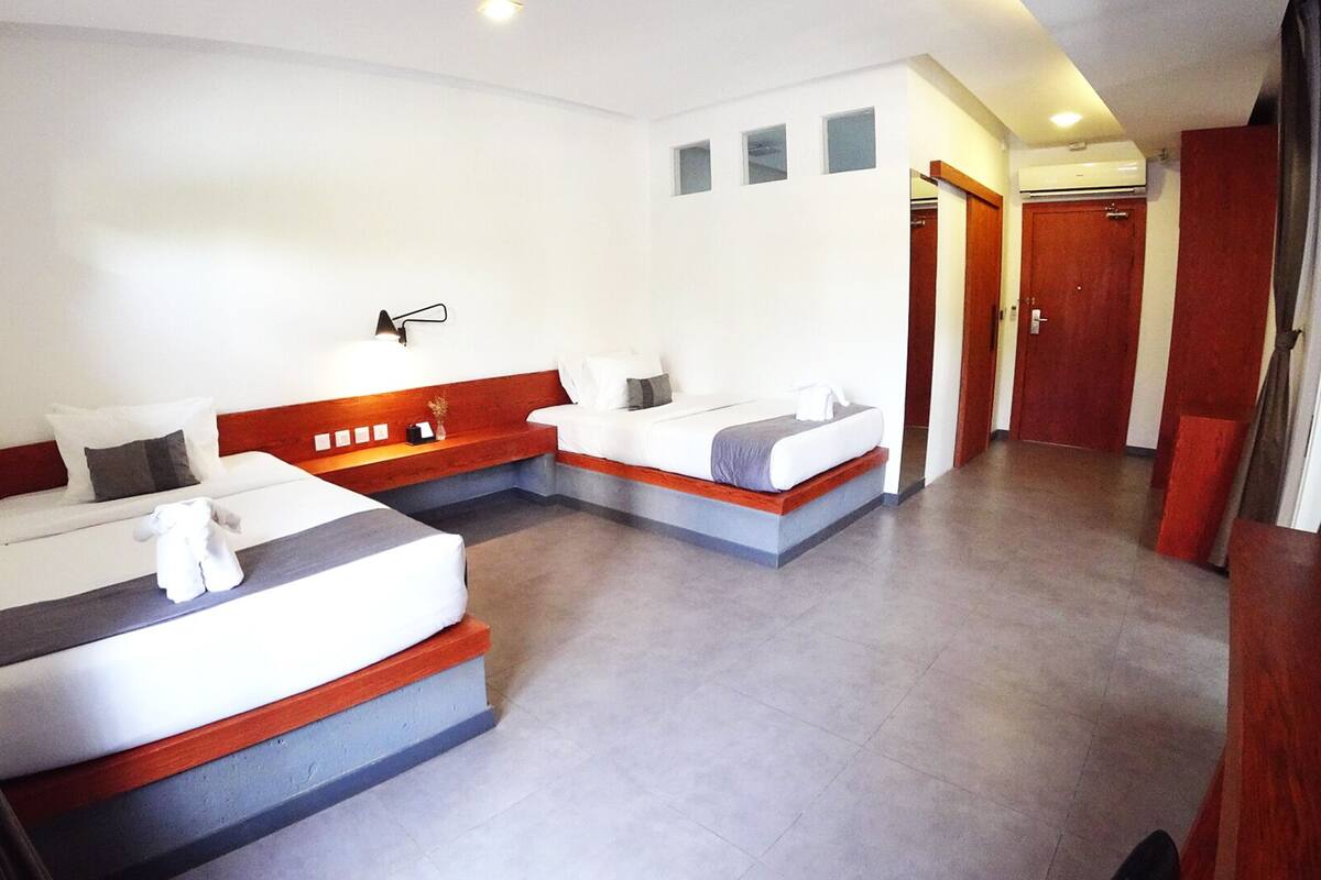 A hotel room with two beds, a small seating area, and a hallway leading to a door.