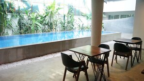 A poolside area with a concrete floor, a pool with clear blue water, and several wooden tables and chairs. - Hotel Records (Phnom Penh)