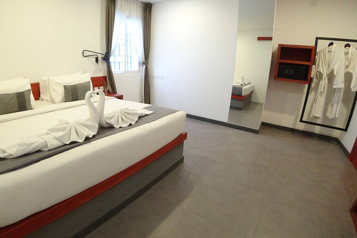 A hotel room with a bed, a mirror, a robe rack, and a window with curtains.