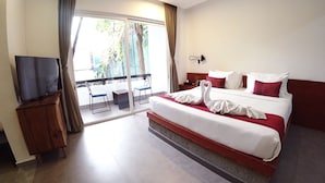 Habitación de hotel con cama, televisión, balcón con sillas y vista a zonas verdes.
